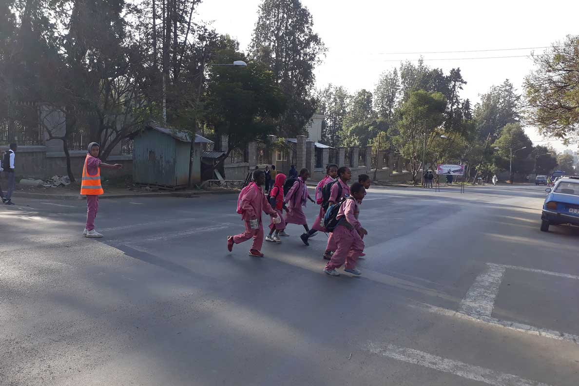 A traffic warden in a hi-vis vest holding traffic while schoolchildren cross the road